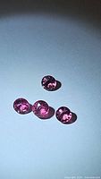 Four individual round cut pink purple tourmaline gemstones displayed on white surface showing brilliant coloration and clarity.