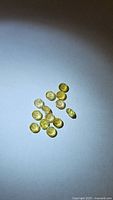 Multiple small round yellow tourmaline gemstones with faceted round cuts laid out on a surface, showing their color and facets