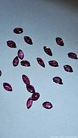 Multiple small marquise cut natural rubies with a deep red-purple hue laid out on a light background.