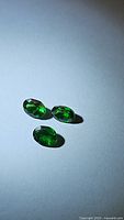 Three vivid green oval cut gemstones arranged on a light surface showing color and cut detail.