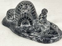 View of entire cast stone sculpture showing igloo, seals, Inuit child, and bird figure on a textured base.
