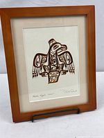 Full view of framed copper-colored embossed print titled 'Haida Eagle Ghuut' by Bill Reid, showing Haida eagle design inside wood frame.
