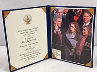 Open blue portfolio showing printed invitation on left and color photo of President Clinton's inauguration on right