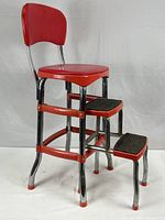 Front and side view showing pinkish red padded seat and backrest, chrome frame, and two steps with black rubber tread.