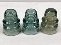 Photo showing three vintage glass electrical insulators side by side on a white surface, highlighting their color differences and size.