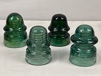 Four blue/green glass electrical insulators arranged in a row, showing their shapes and colors.