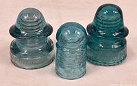 Three blue glass electrical insulators shown together on a white surface, different shapes, heights, and embossed markings visible.