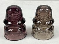 Pair of two vintage glass electrical insulators, side by side, showing two distinct amethyst shades and the embossed 'CALIFORNIA' marking on the base