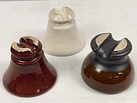 Photo of three porcelain electrical insulators, white unmarked, brown '825' marked, brown/black 'Japan' marked