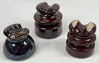 Three dark brown porcelain electrical insulators arranged together showing various shapes and sizes.