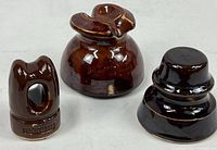 Set of three brown glazed porcelain electrical insulators with varied shapes and sizes