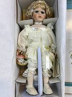 Porcelain doll in lace dress with blonde hair and blue eyes inside original box.