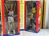 Two boxed fully poseable basketball figures of Charles Barkley in a black and white Houston Rockets uniform and Shaquille O'Neal in a yellow Los Angeles Lakers uniform, each about 14 inches tall.