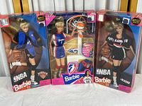 Three Barbie dolls in original packaging showing distinct NBA and WNBA team uniforms with plastic window boxes.
