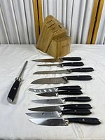 Complete view of 9 kitchen cutting tools and sharpening steel laid out next to bamboo knife block with angled slots and Saveur branding.