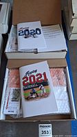 Two open boxes each containing a Baseball Replay game set for 2020 and 2021, showing rule books and bubble wrapped contents.