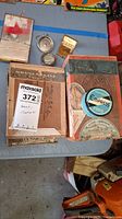 Photo showing 5 vintage cigar boxes with varying wear and three small metal compacts, one compact is a blue Empress Typewriter Ribbon tin.