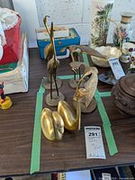 Six brass bird figurines on a wooden table, a mix of cranes and swans in varying sizes and poses. Background shows other vintage items.