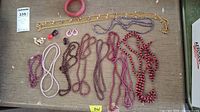 View of all costume jewelry items arranged on table including multiple beaded necklaces, gold-tone chain, bracelet, earrings, and rings