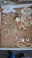 Tray with assorted costume jewelry including multiple pearl bead necklaces, bracelets, earrings, floral pins, and white beaded balls in a plastic bag.