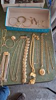 Overview of various gold-tone costume jewelry laid out on a green surface including necklaces, bracelets, earrings, and pendants.
