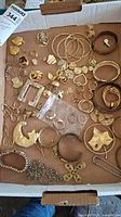 Full view of the assorted gold-tone costume jewelry pieces including bracelets, rings, earrings, and pins laid out in a box.