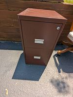 Front view of the brown two drawer metal filing cabinet showing the two drawers with metal handles and lock area.