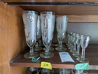 Shelf containing 10 pilsner glasses and 6 cordial glasses with silver leaf designs and silver rims.