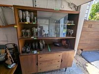 Front view of the Mid-Century Modern hutch showing glass sliding doors on top, three central drawers, and two lower doors. Glassware and decorative items inside are excluded.