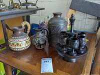 A table holding three pottery pitchers or vases and a wooden cordial glass set with stand, showing overall lot contents.
