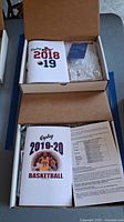 Box containing the 2018-2019 and 2019-2020 Replay Basketball sets including binders and printed materials.