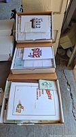 Top-down view of three open boxes containing printed baseball play set materials including yearbooks and cards from 2002, 2013, and 2019.
