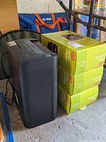 Paper shredder front and side view with stickers and power cord visible alongside green Staples file cases boxes stacked
