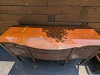 Full view of wooden sideboard showing curved front, two dovetailed drawers, side storage compartments, scratches and wear on surface finish.