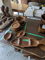 Wooden carved dishes and trays displayed on table, including serving spoon and various trays with natural wood grain visible.
