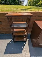 Full front view of wooden shelving unit outside, showing four shelves and overall structure, some surface wear visible.