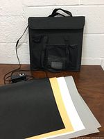Foldable carrying case with handle, power cord and light switch, and four colored backdrop sheets (black, gold, white, gray) laid out in front
