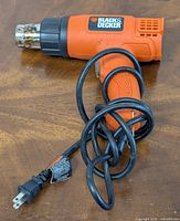 Full view of Black & Decker heat tool showing orange and black body with power cord coiled in front.