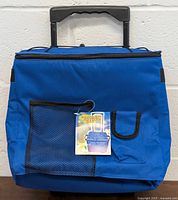 Front view of bright blue foldable trolley cooler with mesh pocket, cellphone pocket, large main compartment, and attached product tag.