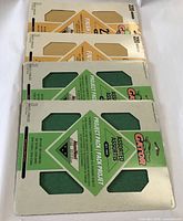Four packs of Gator sandpaper, two packs with 220 grit, beige and orange packaging, and two green packs labeled as assorted grit 80-120-220, each pack containing 3 sheets sized 9x11.