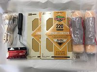 Photo of 6 bundled paint brushes, 2 paint rollers with orange rollers, pack of sandpaper sheets, and a paint roller handle.