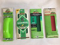 Lot contents arranged side-by-side including the green clamp-on Gator hand sander and three packs of sandpaper sheets of various grits.
