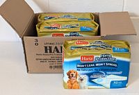 Three packs of Hartz Home Protection Dog Training Pads inside an open cardboard box, showing packaging with product branding and images of dog and cat.