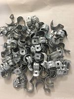 Multiple 3/4 inch one hole EMT straps piled together showing galvanized steel finish and design.