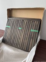 Folded table panels showing dark wood slats with protective green tape, inside cardboard packaging.