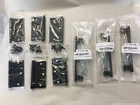Six black steel hinges with screws and three black cabinet handles sealed in bags, all new.