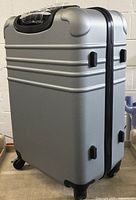 Side view of the silver hard shell suitcase showing the textured surface, wheels, and side handle.