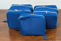 Front view showing six of the eight identical blue toiletry bags with zipper closures placed on a wooden surface.