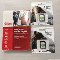 Two individually packaged Kingston 64GB Canvas Select Plus SD cards in blister packs with photos on packaging. Next to them is a sealed pack of Office Depot multi-project gloss photo paper containing 50 sheets of 4x6 inch size.