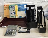 Image showing all items including file holders, paper tray, labels, calculator, and stapler on a table against a gray brick wall.